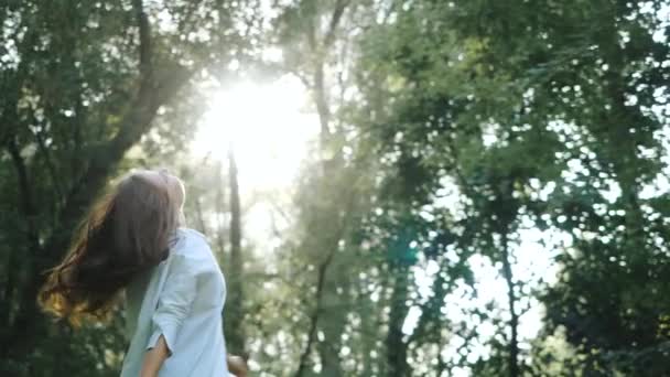 Vue frontale mouvementée d'une jolie fille en chemise blanche qui tourne en rond dans la rue parmi les arbres du parc. Heureuse belle femme souriante a organisé une séance photo dans l'air frais par temps ensoleillé . — Video