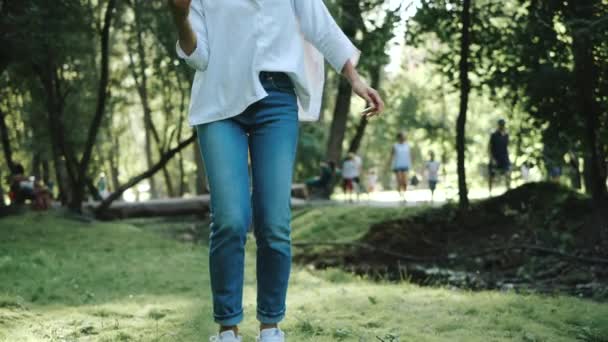 暖かい週末に都市公園の芝生の上に立つ魅力的なかわいい女の子のつま先のショットに向かいます。ジーンズの美しい女性と白いシャツは暖かい晴れた日に新鮮な空気中のカメラのポーズ. — ストック動画