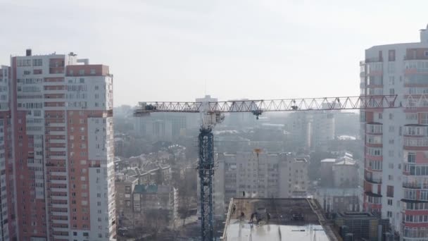 La construcción de un edificio moderno de gran altura con la ayuda de una grúa elevadora en un sitio de construcción, vista superior. Trabajadores de pie en el techo y construir un nuevo piso de la casa, Jarkov, Ucrania. — Vídeo de stock