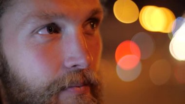 Yakından bakınca, yakışıklı, beyaz sakallı, uzun saçlı genç bir adamın portresi düz görünüyor ve hareketli bir şehrin arka planında gülümsüyor..