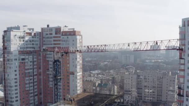 Draufsicht auf einen Hebekran für den Bau eines neuen Hochhauses im Stadtzentrum von Charkow, Ukraine. Arbeiter stehen auf dem Dach und bauen inmitten schöner Bürohäuser im Winter ein modernes Gebäude. — Stockvideo