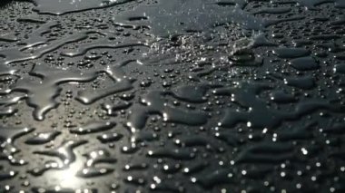 Yağmur, grafit renginin pürüzsüz parlak yüzeyine, küçük su havuzlarıyla kaplı olarak yağar. Güneş ışığı ve ışık birikintilerinden yansıma. Yağmur damlaları sabah dışarıda yere düşer. Yağmurlu hava.