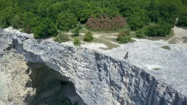 Top pohled na zkušeného a aktivního mužského turistu, který běží v blízkosti útesů hory a má výhled na přírodu lesů. Extrémní sportovec běhá podél úpatí hory. — Stock video