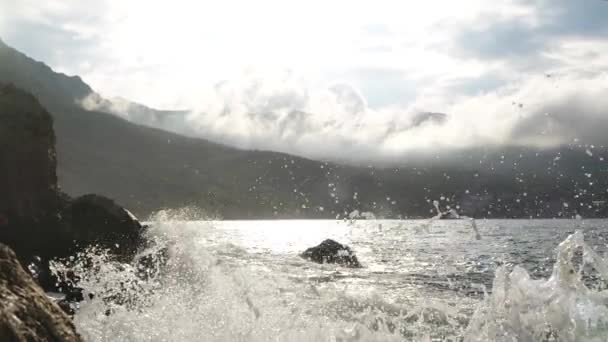 Belos salpicos de ondas do mar em clima quente ensolarado contra o pano de fundo de nuvens longas flutuantes que se assemelham a fumaça espalhada, a Crimeia. As ondas do Mar Negro estão quebrando nas rochas durante a tempestade — Vídeo de Stock