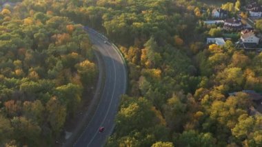 Sonbaharda güzel renkli ormanın hava görüntüsü. Köy yolunun üst köşesinin manzarası. Sonbaharın güzel doğası ormanda bir yürüyüşe ilham verir. Ağaçların arkasında yollar ve zengin evler.