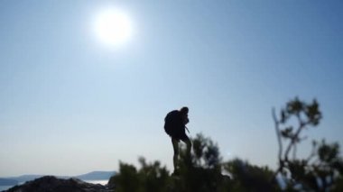 Sırtında sırt çantasıyla bir uçurumun tepesinde ağır çekimde yürüyen genç bir kızı sırtından vurmak. Atletik kadın, açık gökyüzündeki parlak güneşin güzel manzarasının tadını çıkarıyor. Denizde olay ışınları var..