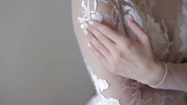 Молода красива європейська наречена в мереживній весільній сукні біжить рукою з манікюром над плечем, обіймає себе, і модель постає для камери в яскравій кімнаті, великий план. — стокове відео