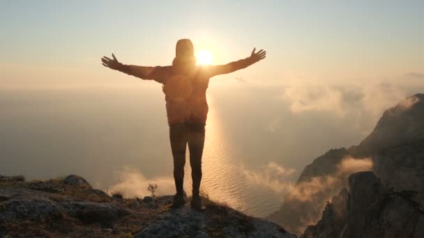 Aktif sakallı adam yüksek bir dağın kenarında kollarını açıp el sallayarak anın tadını çıkarıyor. Atletik erkek turist, denizde gün batımının arka planında bir uçurumun kenarında duruyor.. — Stok video