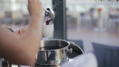 Garson, sabahki ziyafet salonunda bir düğün davetlisi için bardağa şarap doldurur. Güzel manikürlü kadın elleri ve kırmızı bir bilezik beyaz bardağı sıcak punçla doldurur..