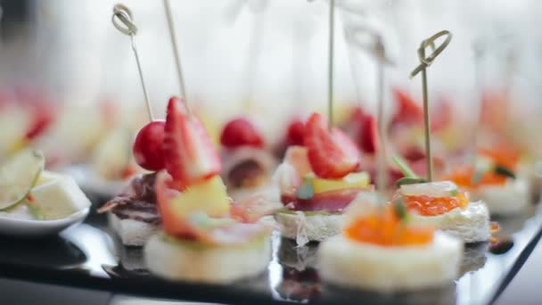 Tiro cerca de deliciosos aperitivos en brochetas con caviar rojo, fresas y rodajas de tocino de pie en una bandeja de mesa negra para los invitados de una fiesta de bodas. Deliciosos aperitivos perd plato principal . — Vídeos de Stock