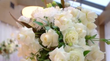 Açık ve taze beyaz güllerin yakın plan çekimi bir vazoda duruyor ve bir düğün partisi için hazırlanıyor. Gelin ve damadın kutlaması için salondaki düğün masasını süsleyen güzel çiçekler..