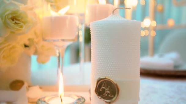 Primo piano di due candele in fiamme in occhiali nuziali che stanno su un tavolo di banchetto vicino a un mazzo di rose gialle di un banchetto nuziale sullo sfondo di luci in fiamme sfocate. cerimonia nuziale . — Video Stock