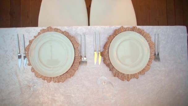 顶部拍摄一对盘子，刀具，叉子和眼镜站在一张有白色桌布和椅子的婚桌上。在新婚夫妇的婚宴上，在大厅里提供简单方便的服务. — 图库视频影像