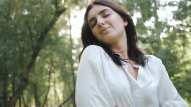 Kadın gözlerini kapattı ve parkın temiz havasını ve doğasını seviyor. Çekici, gülümseyen, uzun saçlı esmer bir kızı yakından çek. Esinti hafifçe eser. Avatar için iyi bir fotoğraf.