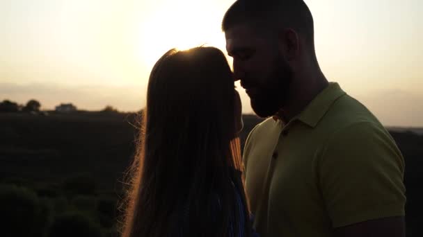 Menina jovem e cara abraçar e beijar na natureza contra o fundo de um pôr do sol na primavera. Amoroso casal feliz desfrutando de uma noite romântica em um campo deserto. Menina agradável beija seu amante, close-up vista. — Vídeo de Stock