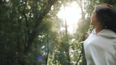 Güzel esmer kız gülümsüyor ve güzel bir fotoğraf için kıvranıyor. Sevimli çekici kız gülümsüyor ve ilkbaharda bir şehir parkındaki ağaçların arasında sıcak bir bahar gününün tadını çıkarıyor. Yakın çekim manzarası. Hafıza için fotoğraf.