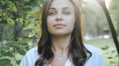 Parkta güneşli bir havada ağaçların arasında duran uzun güzel saçlı güzel bir kızın yanında. Baharda temiz havadan ve parkın doğasından hoşlanan genç bir kadının yüzüne odaklanıyorum.