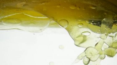 Beyaz arka planda keten tohumu ve susam yağı karışımı. Su dolu altın sıvıyı cam bir kaseye boşalt, yakından bak. Ayçiçeği yağı suda guruldar ve hava kabarcığı oluşturur..