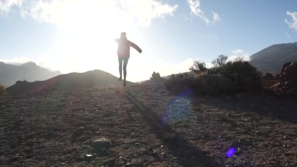 Sporty ragazza felice escursioni turistiche a scogliera di bassa montagna, rimbalza e allarga le braccia al lato di godere del bellissimo paesaggio della natura desertica sotto il sole, vista posteriore. Tempo libero sano — Video Stock