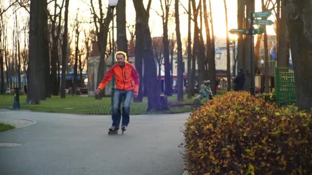 年轻的长毛胡子男子轮滑运动员在城市公园的一个美好的夜晚在圆锥之间跳舞。慢动作在圆锥体之间自由式滑轮滑. — 图库视频影像