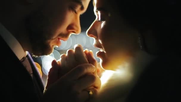 Happy wedding couple is standing on restaurant terrace in the evening holding hands in cool air. Bearded groom holds his beloved bride by arms and blows her in the palm of his hand to warm under light — Stock Video