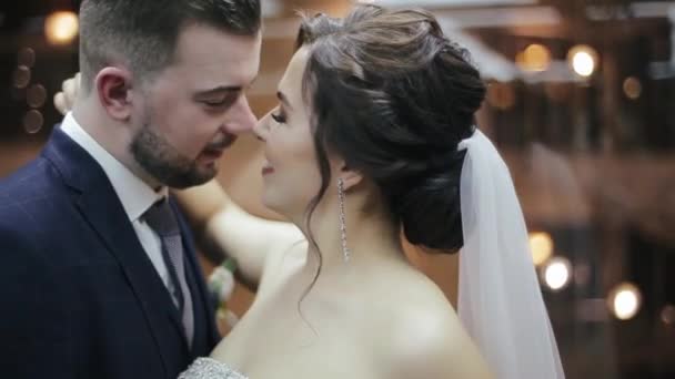 Gelukkige bruid en bruidegom in trouwjurken rijden in de hotel lift, knuffelen en kussen. Vrouw met boeket bloemen en trouwjurk en man met baard in een pak strelen elkaar in een moderne lift. — Stockvideo