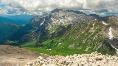 Rusya 'nın güneşli bir ilkbahar gününde, devasa kümülüs bulutlarının altında kar ve otlarla kaplı güzel Adigea dağlarının çarpıcı panoramik zaman çizelgesi. Yeşil vadide doğa manzarası.
