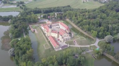 Ağaçların arasında yer alan sıcak ve güneşli havada eski Nesvizh Kalesi 'nin güzel manzarası. Belarus 'un tarihi şatosunun su dalgaları üzerinden ağır çekimde çekilmiştir..