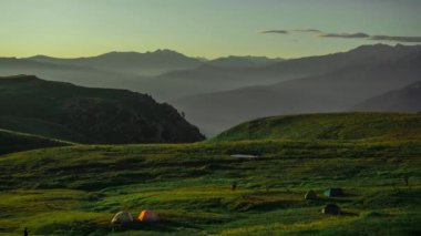 Çimenlerle kaplı bir dağın güzel manzarasının havadan hızlandırılmış çekimi, çadırlı turistler. Zaman aşımına uğramış doğa, insanlar Rusya 'nın Adygea kentindeki bir dağda yürüyorlar..