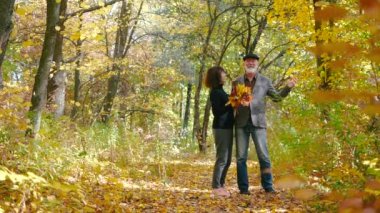 Mutlu, yaşlı, sakallı bir çift ve bir buket yaprakla gülüyor, yürüyüş yapıyor ve ağaçların arasında sıcak bir sonbahar ormanında birlikte vakit geçiriyorlar. Son sınıf öğrencisi yaprakları sarıyor..