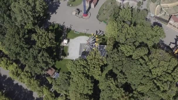 Vue de dessus de Gorky Central Park à Kharkov, Ukraine, bordée de nombreux arbres avec divers manèges passionnants sur lesquels les gens roulent en ville par temps chaud et ensoleillé du printemps. Parc d'attractions pour les loisirs, plan aérien — Video