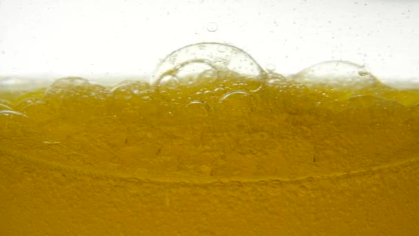 A közeli kilátás a finomítatlan napraforgóolaj a táplálkozás, amely a keverés kezdett alakulnak buborék szerkezete levegő. Arany folyadék lassan keverve olívaolajjal fehér alapon. — Stock videók