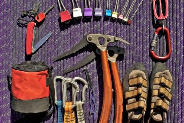Climbing equipment laid out on purple rope. Pocket knife with fire starter, climbing nuts (stoppers), belay/rappel device with carabiner, climbing shoes, ice tools, but tool, quickdraws and chalk bag. clipart