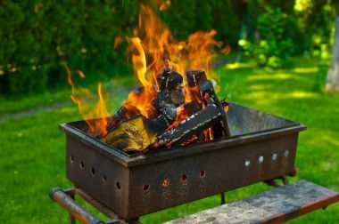 Bir barbekü ızgara yanan odun. Yeşil çim ve ağaçların içinde belgili tanımlık geçmiş.