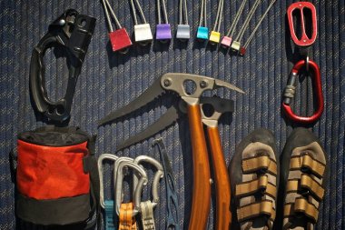 Climbing equipment laid out on a blue rope. Ascender, climbing nuts (stoppers), belay/rappel device, climbing shoes, ice tools, nut tool, quickdraws, chalk bag. clipart