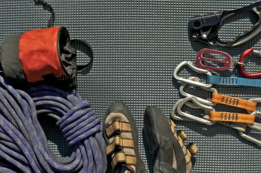 Top view of rock climbing equipment on grey mat. Chalk bag, rope, climbing shoes, belay/rappel device, carabiner and ascender. Active lifestyle concept. clipart