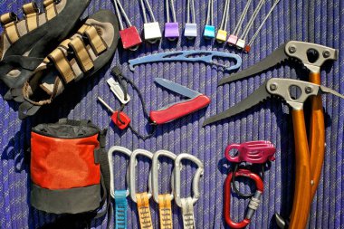 Climbing gear laid out on a blue rope. Climbing shoes, climbing nuts (stoppers), nut tool, ice tools, belay/rappel device with carabiner, quickdraws, chalk bag and pocket knife with fire starter. clipart
