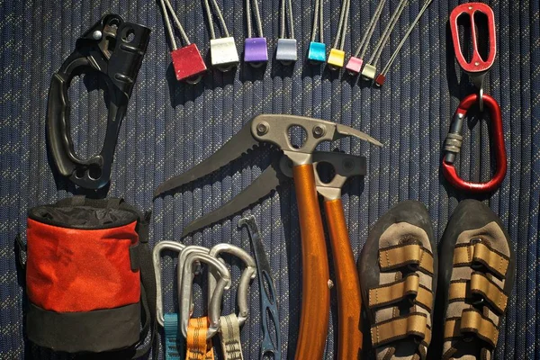 Climbing equipment laid out on a blue rope. Ascender, climbing nuts (stoppers), belay/rappel device, climbing shoes, ice tools, nut tool, quickdraws, chalk bag.