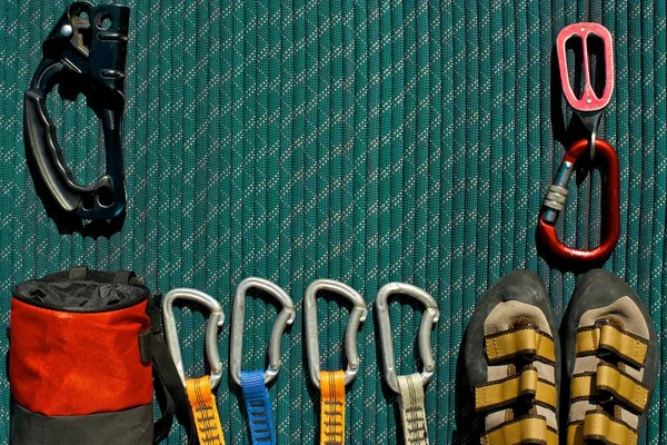 Top view of rock climbing gear laid out beautifully on a green rope. Ascender, chalk bag, quickdraws, climbing shoes and belay/rappel device with carabiner.