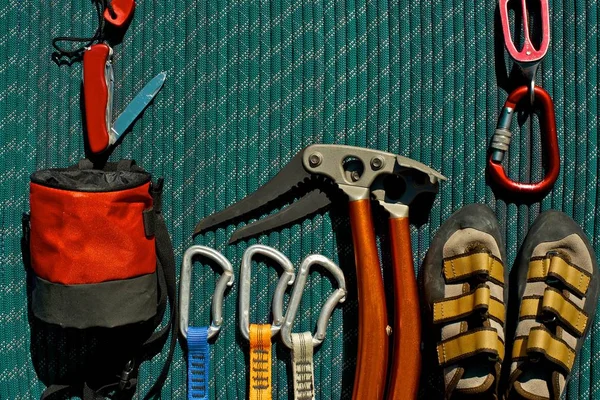 Climbing gear arranged beautifully on a green rope. Pocket knife with fire starter, belay/rappel device with carabiner, climbing shoes, ice tools, quickdraws and chalk bag.