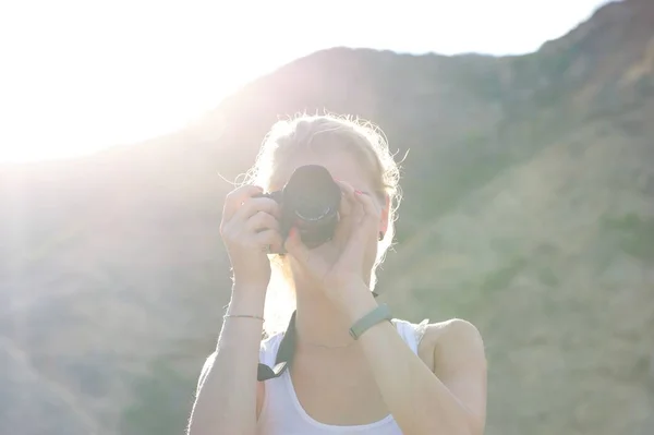 Genç bir kadın fotoğraf çekmek; gizli kamera yüz; parlak güneş ve onun arkasındaki tepeler.