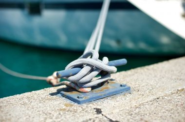 Yacht moored in marina.A closeup picture of a mooring bollard with a rope tied to it.  clipart