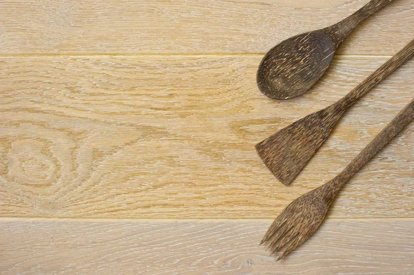 A set of two wooden spatulas and a spoon laid out on light wooden background.