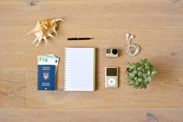 Ready for a walk. Top view of objects of a wooden background: notepad and pen, music player and earphones, passport and money, action camera and seashell and a plant as side pieces.