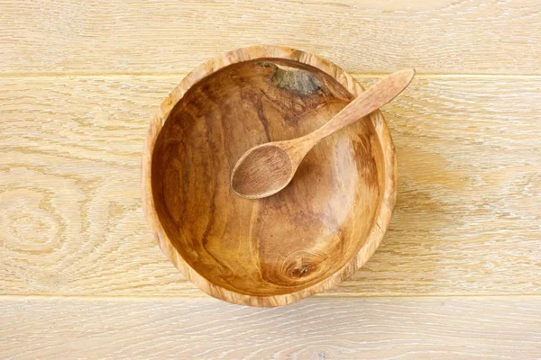 A wooden spoon in a wooden bowl on a wooden background. Top view.