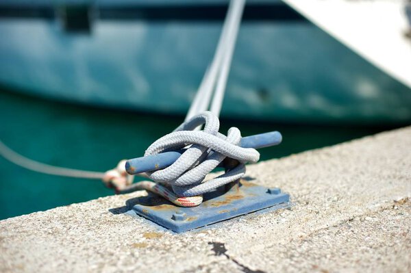 Yacht moored in marina.A closeup picture of a mooring bollard with a rope tied to it. 