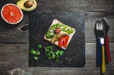 Avokado, greyfurt ve badem pul ile organik tost. Arduvaz black tabak, çatal, ahşap gri arka plan, üstten görünüm