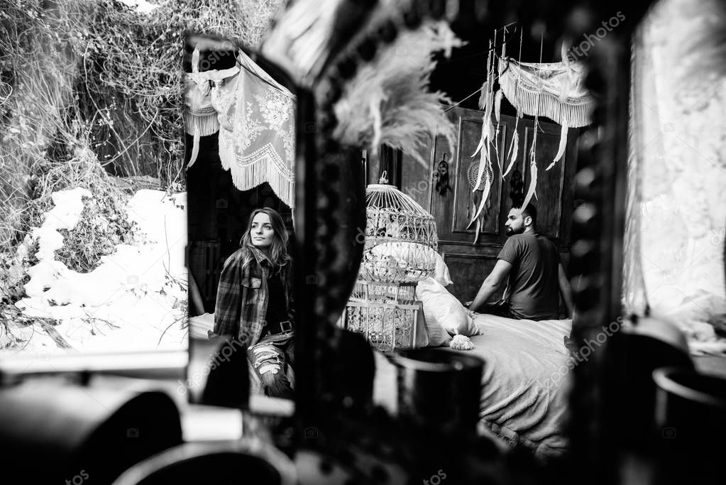 Reflection of the woman in the mirror, she looks out the window. Man sitting on a bed and looking at his woman. Black and white photo, reflection. Love story