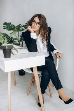 Modern iş bir iş takım elbise ve bir gözlük şık parlak ofisinde bir sandalyede oturur kadındır