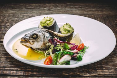 Fırında Alabalık, otlar, domates, limon ve ahşap eski masa üzerinde yuvarlak beyaz tabakta soslu ıspanak püresi ile. Yan görünüm